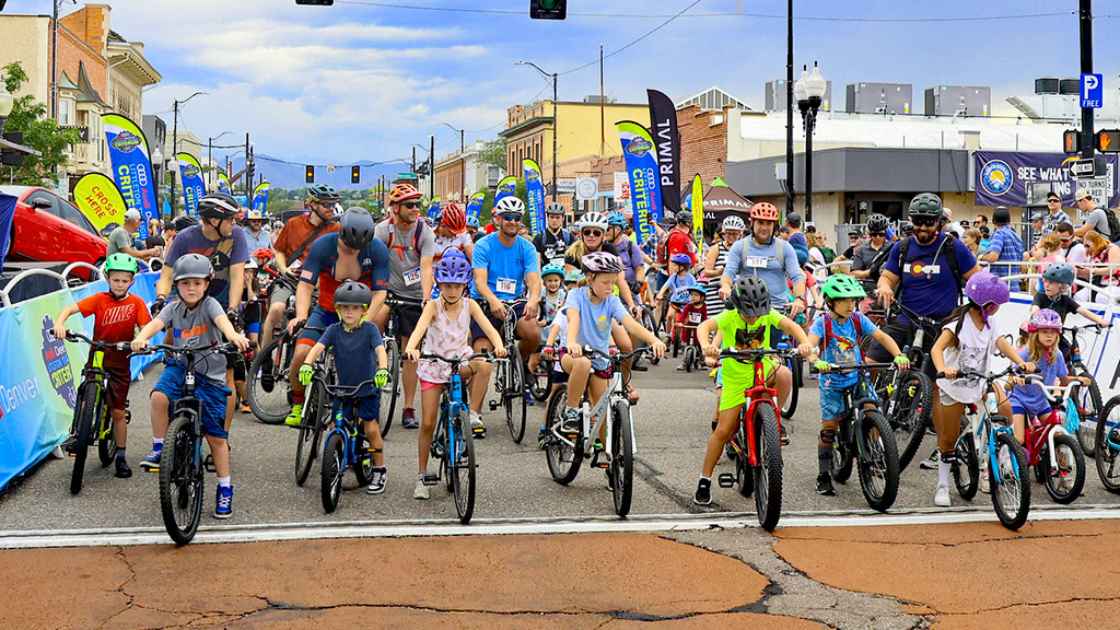 Adults and children wearing helmets ride bicycles on a sunny street.