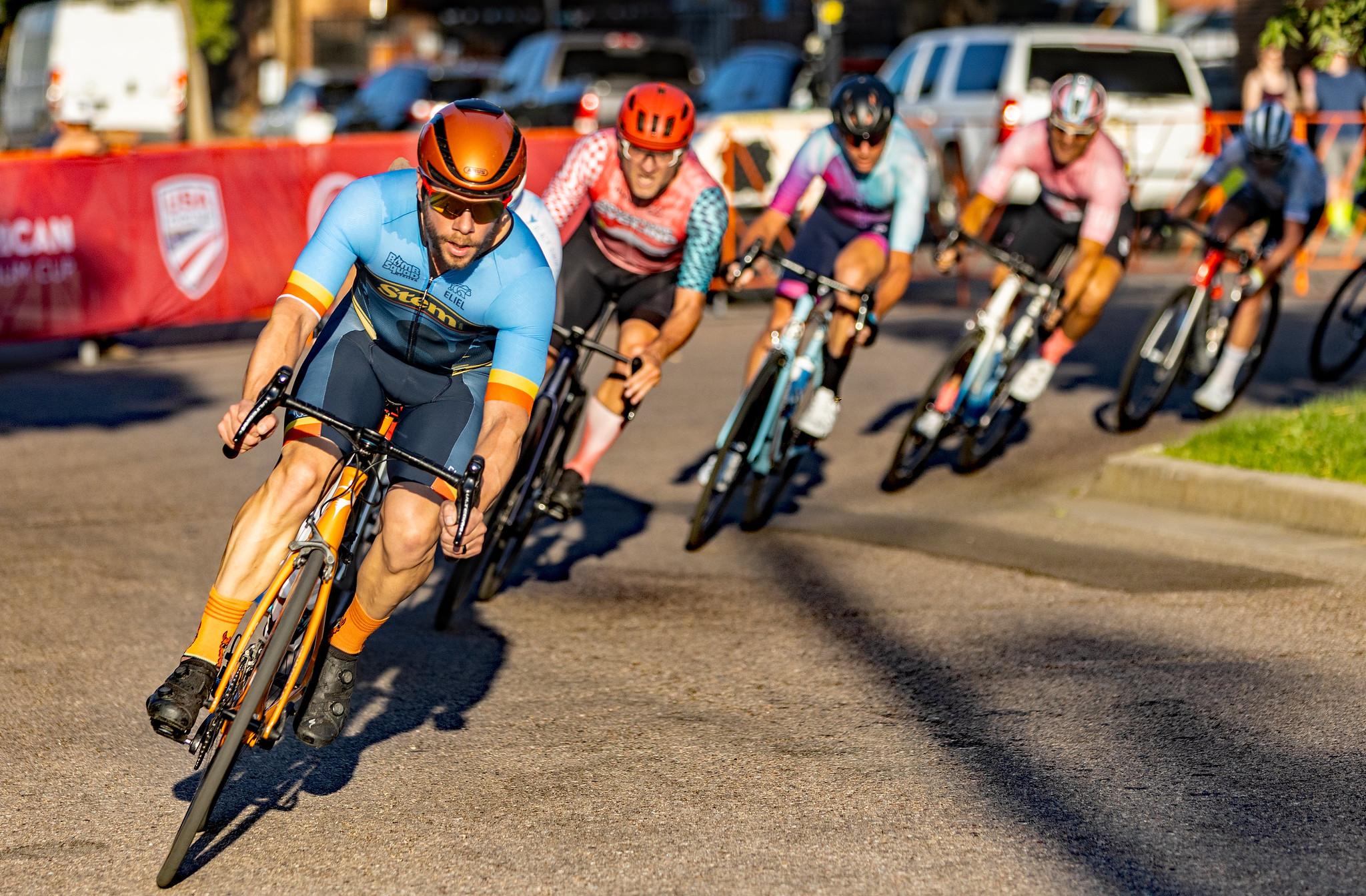 Five cyclists race around a corner on a sunlit city street during a cycling competition.